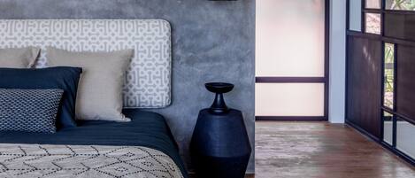 Un dormitorio moderno con un cabecero estampado, una colcha azul oscuro y un cojín de diseño geométrico.