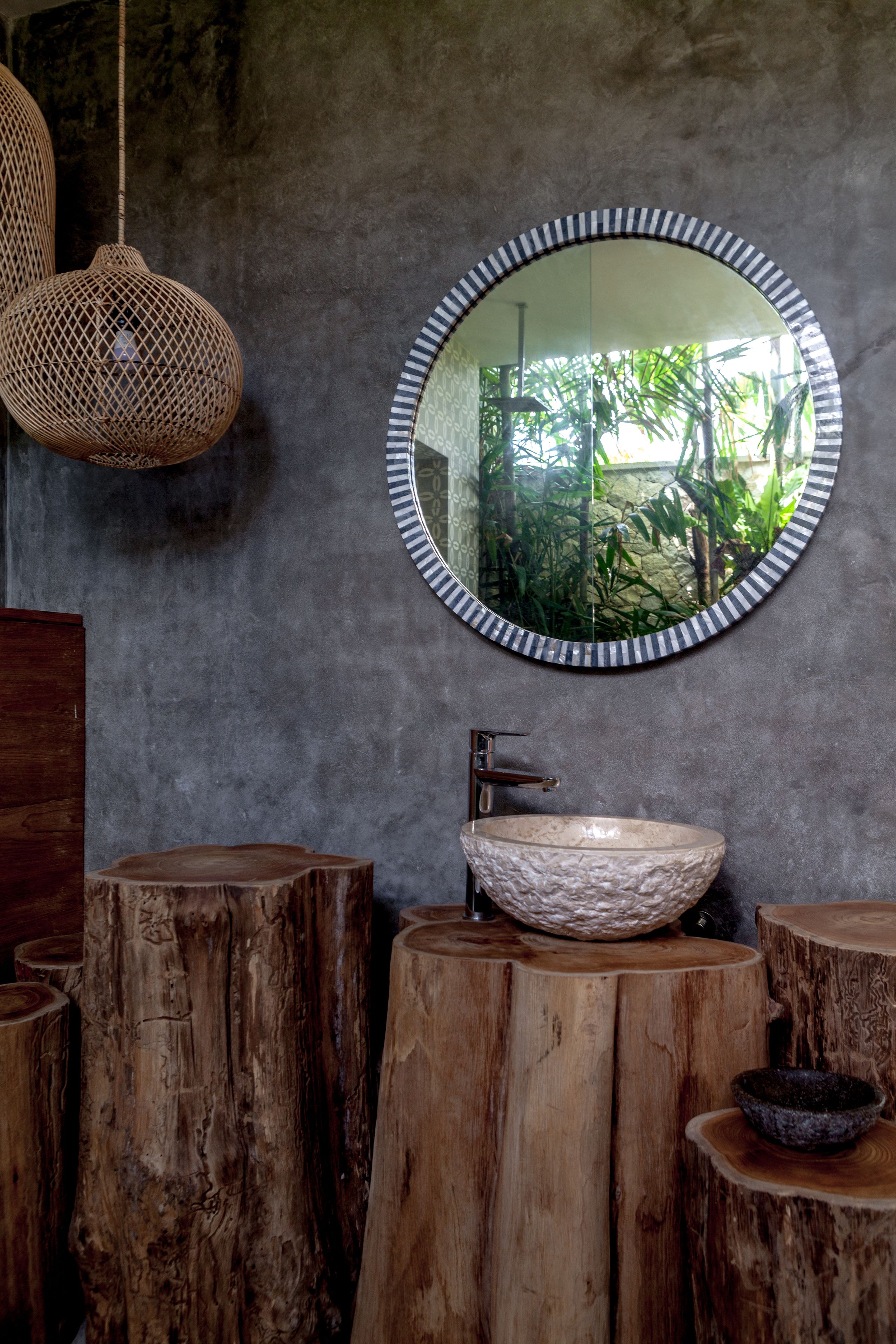 A bathroom with a round mirror, a stone sink, and wooden stools.