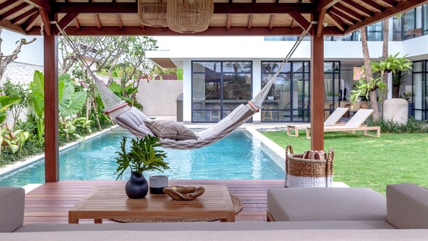 Un hamac sous une pergola en bois, près d’une piscine, avec vue sur une maison moderne.