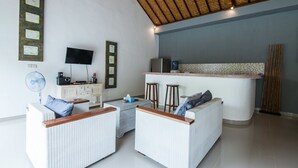 Uma sala de estar moderna com móveis de vime, uma TV de tela plana e bancada de cozinha.