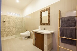 A bathroom with a toilet, sink, mirror, and shower. - Casaluna Villa (Seminyak)