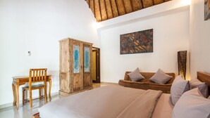 Quarto com uma cama grande, guarda-roupa de madeira, escrivaninha com cadeira e sofá marrom com almofadas.