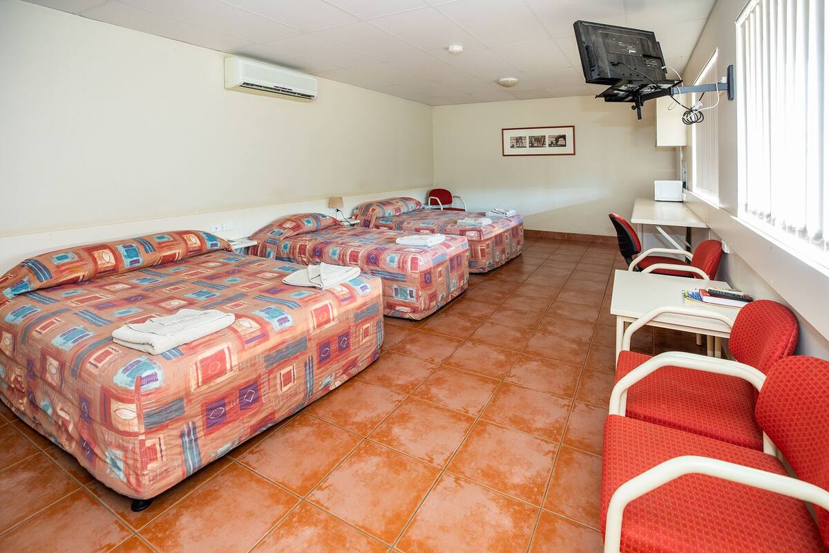 A hotel room with three beds, a desk, and a chair.