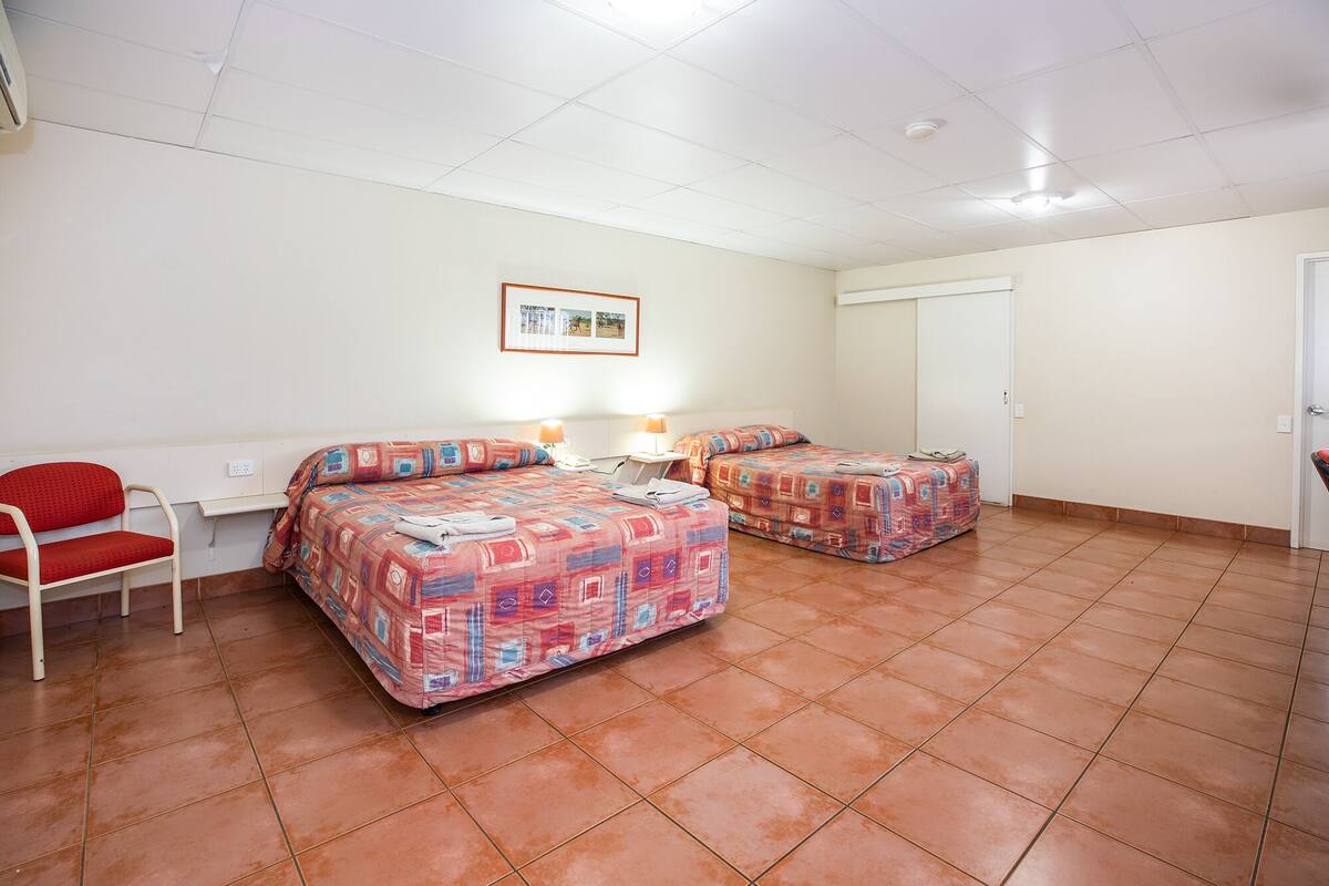 A room with two beds, a chair, a desk, and a framed picture on the wall.