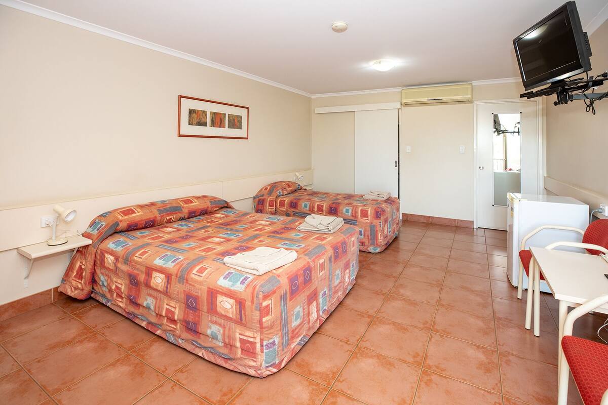 A hotel room with two beds, a desk, a chair, a television, and a door leading to a bathroom.