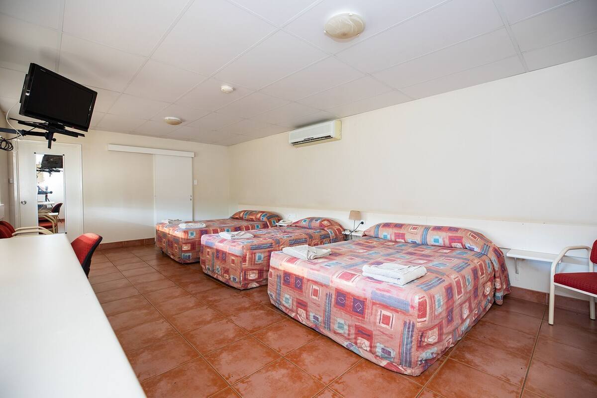 A room with three beds, a TV, and a desk.