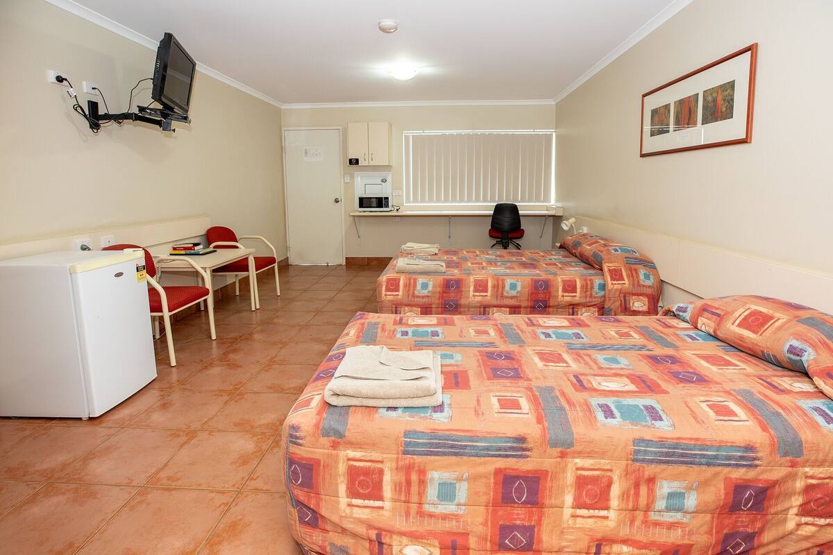 A room with two beds, a desk, a chair, a television, and a refrigerator.