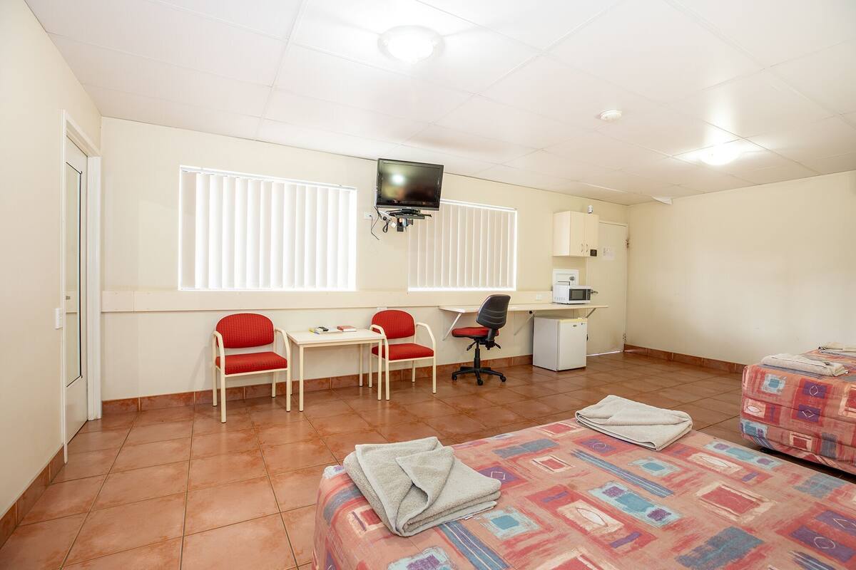 A bedroom with a bed, two red chairs, a desk, a television, and a microwave.
