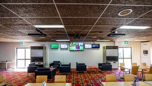 A conference room with multiple tables and chairs, a patterned carpet, and three screens on the wall. - Leichhardt Hotel Motel (Cloncurry)
