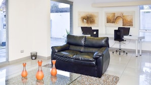 A modern office space with a black leather sofa, two orange vases, and two laptops on a desk. - Bellavista Spotlight Apartment (Santiago)