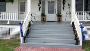 Eine Veranda mit weißer Brüstung, eine Treppe, die zu einer Tür führt, und je einen Blumentopf auf beiden Seiten der Tür.