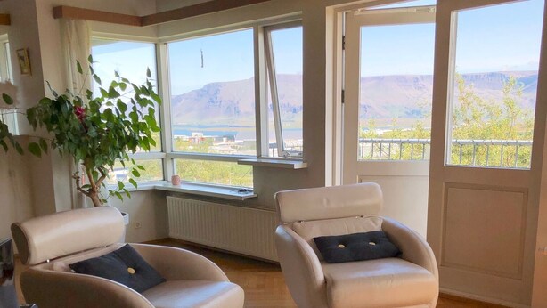 A modern living room with two beige armchairs, a white coffee table, and a large window offering a mountain view. - A spacious house with amazing view (Grafarvogur)