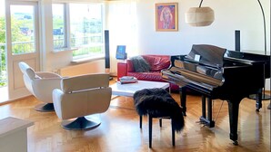 A spacious living room with a wooden ceiling, a grand piano, a red sofa, and a modern chair. - A spacious house with amazing view (Grafarvogur)