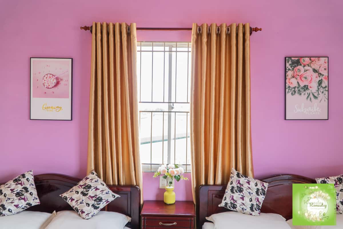 Une chambre avec deux lits, une fenêtre avec des rideaux et un vase de fleurs posé sur une table de chevet.