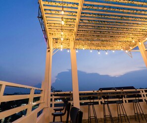 An outdoor seating area with a pergola covered in string lights and a view of the city skyline. - Orchid Garden Homestay Can Tho (Can Tho)