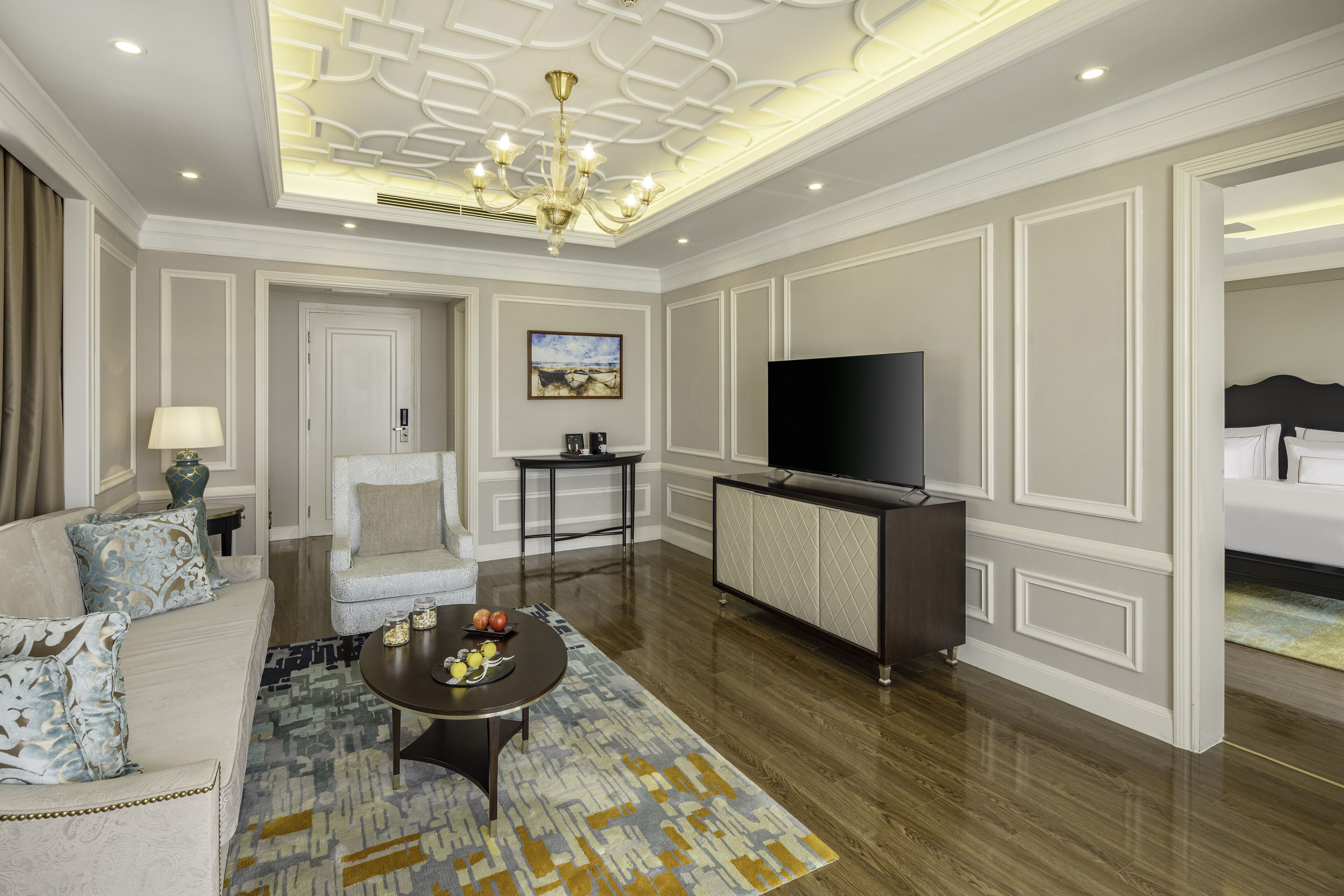 A modern hotel room with a sofa, armchair, coffee table, TV, and a bed.