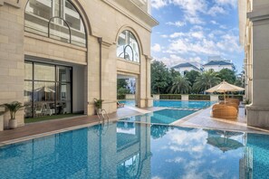 A swimming pool area with a lounge chair and umbrella, a glass door entrance, and a view of the surrounding buildings. - Meliá Vinpearl Hai Phong Rivera (Hai Phong)