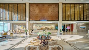 Un hall d’entrée spacieux avec une table ronde centrale, un coin salon avec des canapés et un mur décoratif orné d’un motif géométrique.