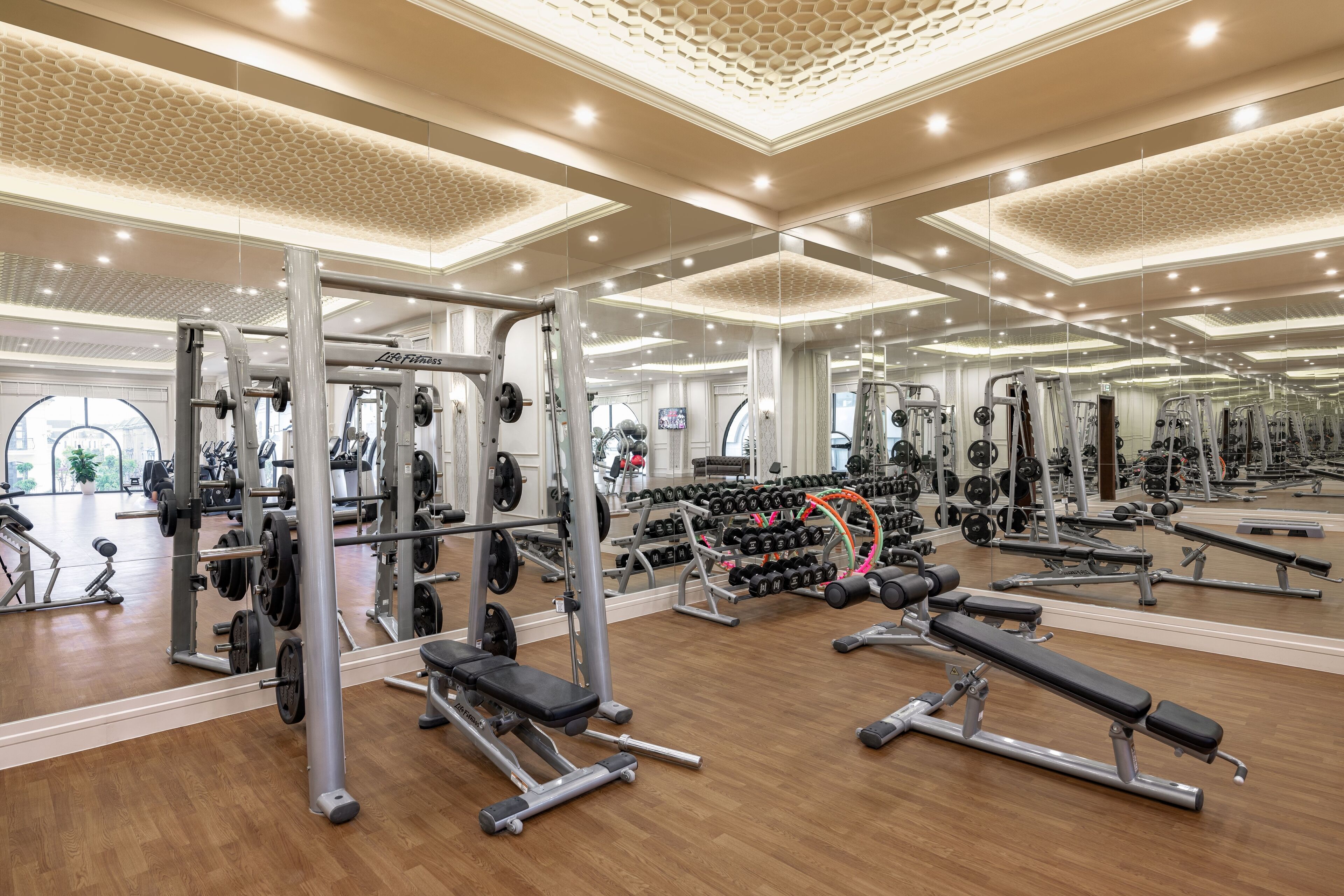 Une salle de sport spacieuse, dotée de divers appareils de musculation, de murs recouverts de miroirs et d’un plancher en bois.