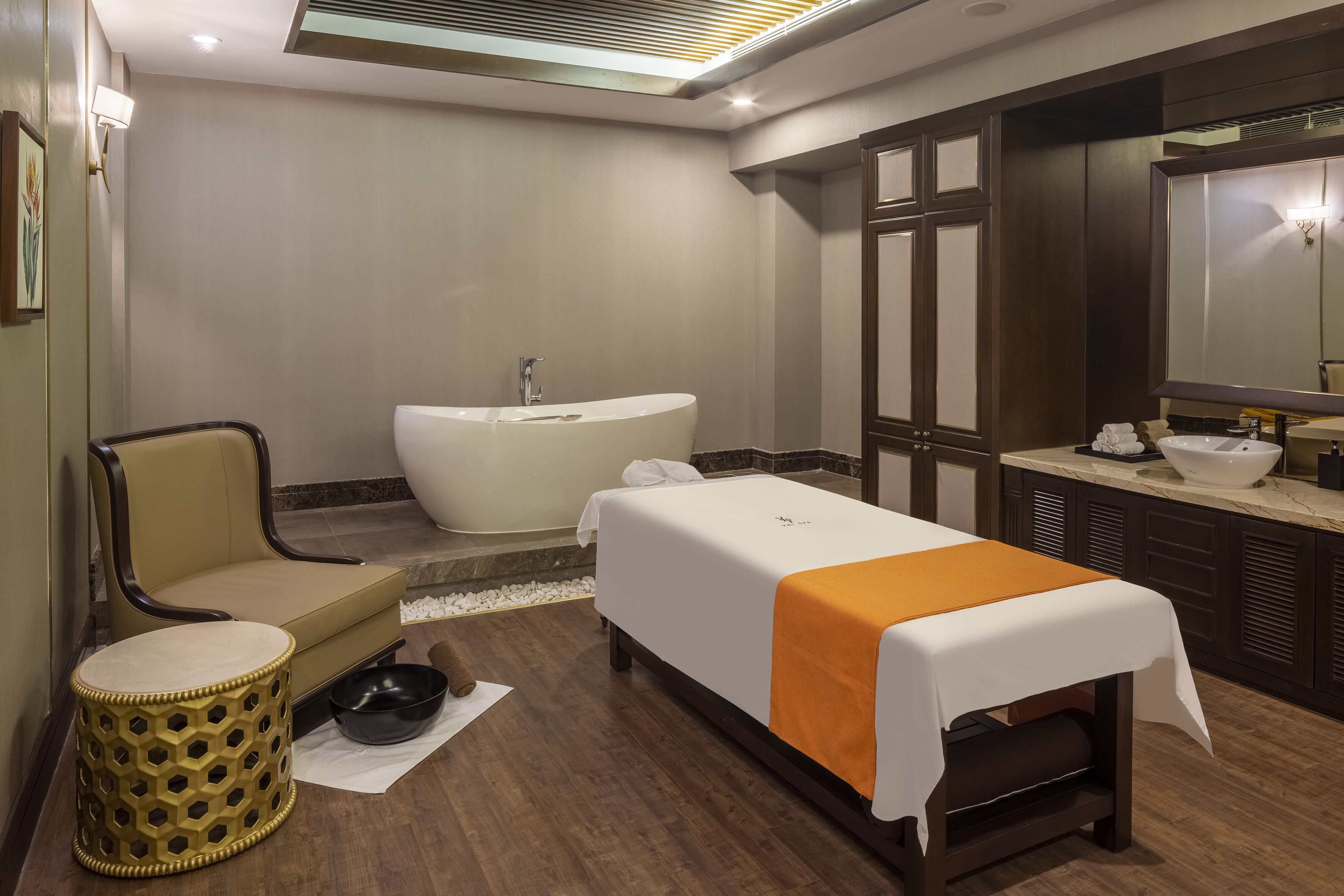 A hotel room with a bed, a bathtub, a chair, a small stool, and a large mirror.