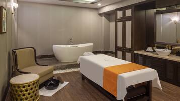 A hotel room with a bed, a bathtub, a chair, a small stool, and a large mirror.