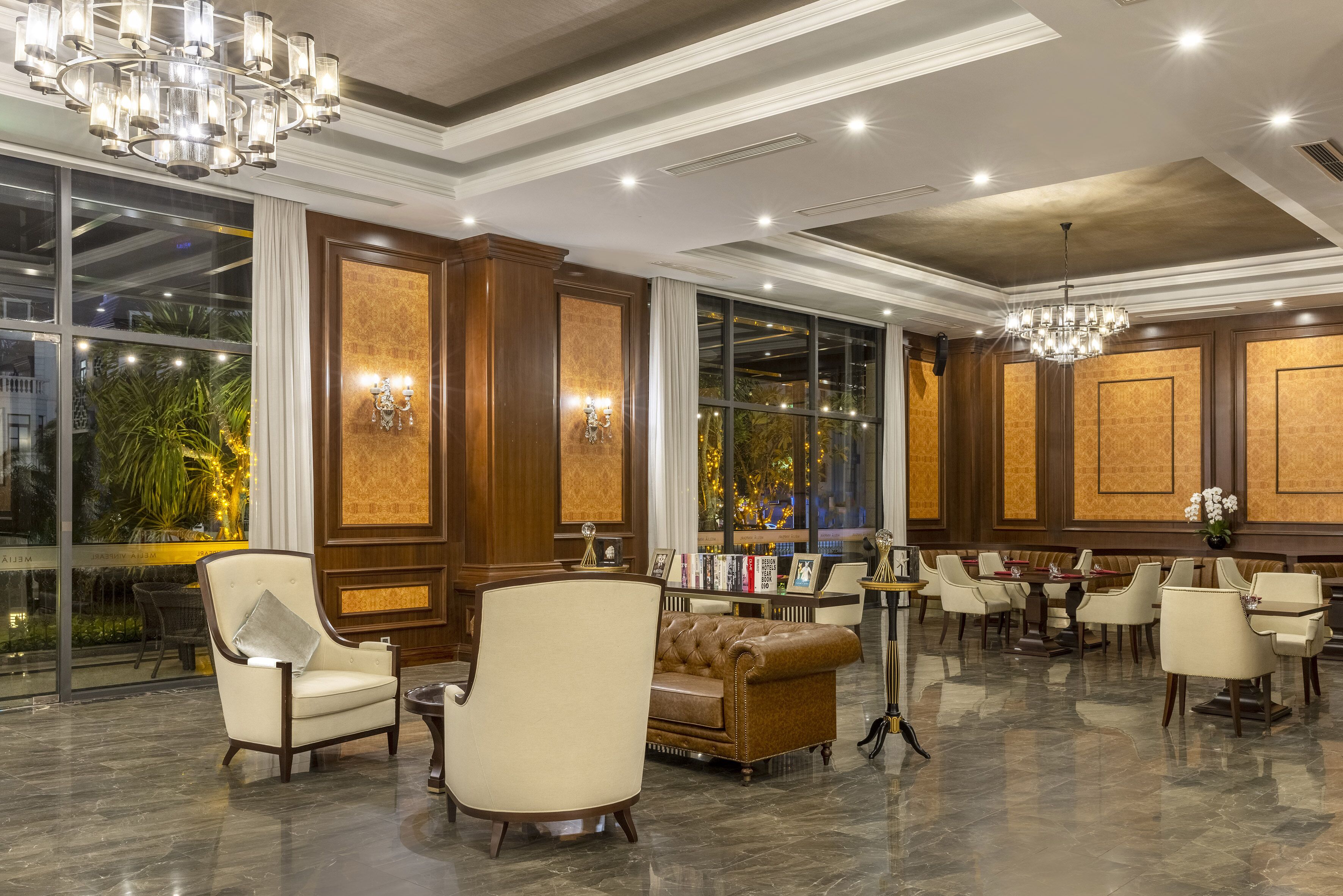 A spacious lobby with a high ceiling, chandeliers, and a seating area with leather sofas and armchairs.