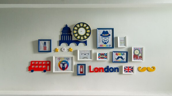 A wall with various framed pictures and decorations, including a clock, a bus, and the word "London".