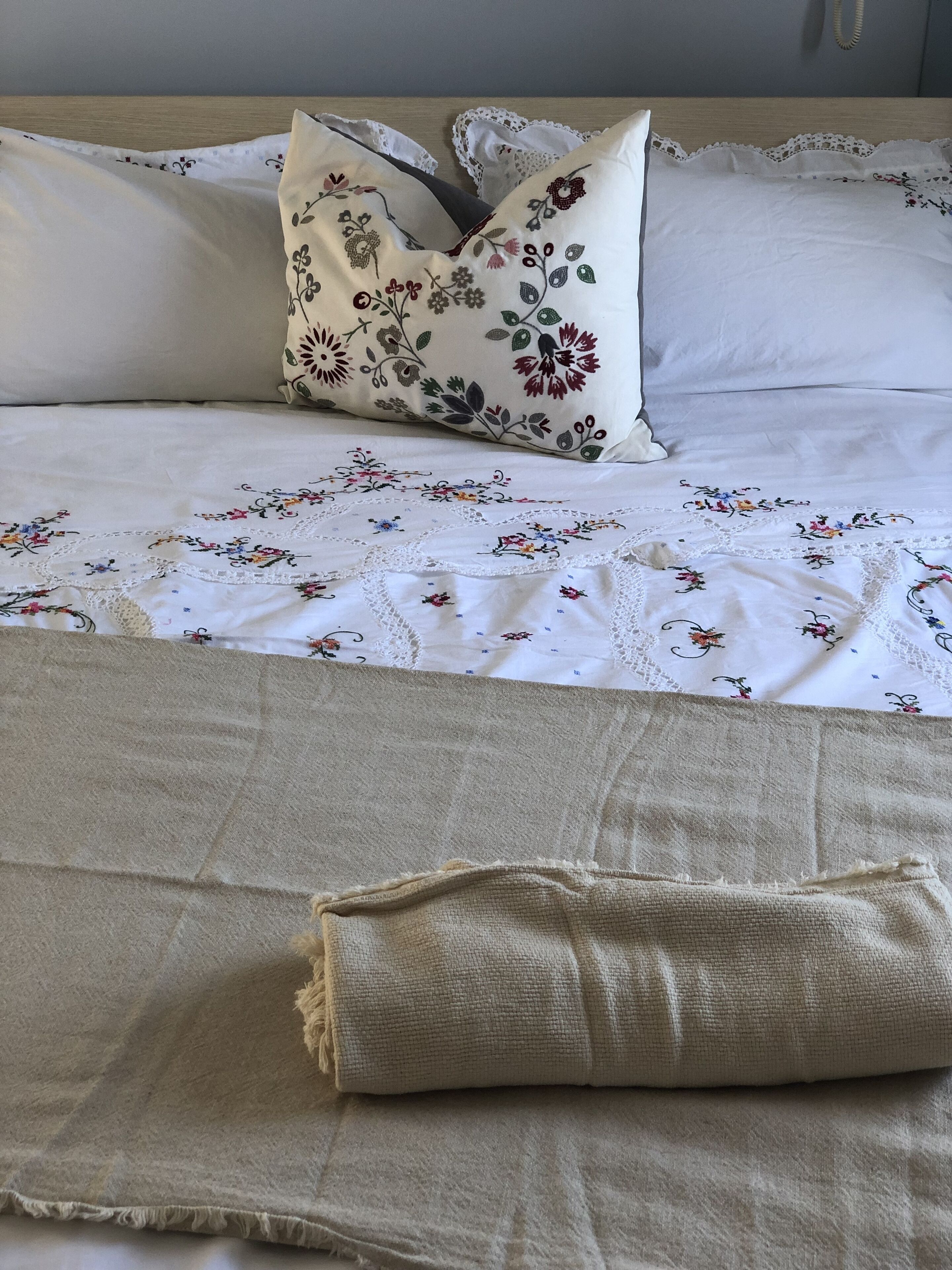 Ein ordentlich bezogenes Bett mit einer blumigen Tagesdecke und einer beigen Zudecke.
