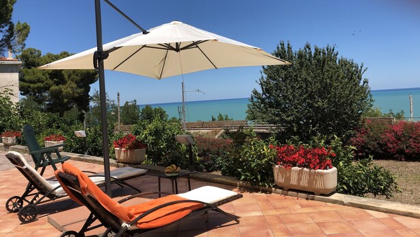 Un patio con una sombrilla blanca, dos sillones de relax y vista al mar.