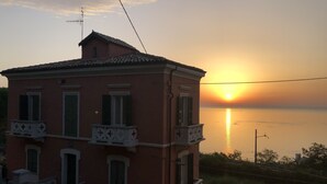 Un edificio rosa con balcón, con vista a una puesta de sol sobre el agua.