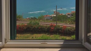 Vista a través de una ventana que muestra una zona costera, cielo despejado, océano y edificios a lo lejos.