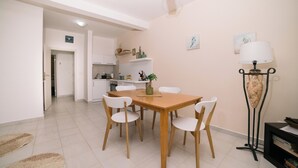 Een eethoek met een houten tafel en witte stoelen, een keuken op de achtergrond, en een lamp aan de rechterkant.