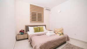 Een slaapkamer met een bed, nachtkastjes, een potplant en een raam met jaloezieën.
