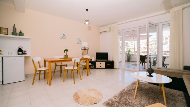 Een moderne woonkamer met een eethoek, een televisie en een balkon met tuinmeubilair.