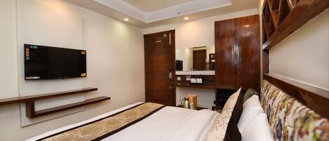 A hotel room with a bed, a television mounted on the wall, a wooden wardrobe, and a mirror.