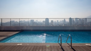 Ein Pool auf dem Dach mit Blick auf die Stadtlandschaft, Metallgeländern und einer Holzterrasse.