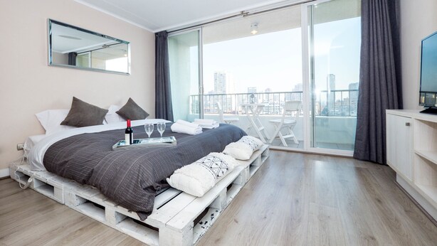 Ein modernes Schlafzimmer mit Bett, Flachbildfernseher und Balkon mit Blick auf die Stadt.