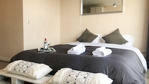 Ein ordentlich bezogenes Bett mit dunkler, gemusterter Bettdecke, zwei Kissen und zwei zusammengerollten Handtüchern.
