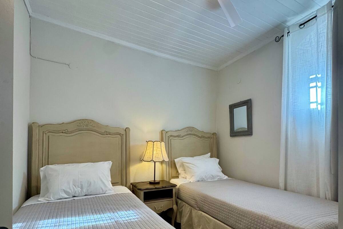 Ein Zimmer mit zwei Betten, einem Deckenventilator, einem Nachttisch mit Lampe und einem Spiegel an der Wand.