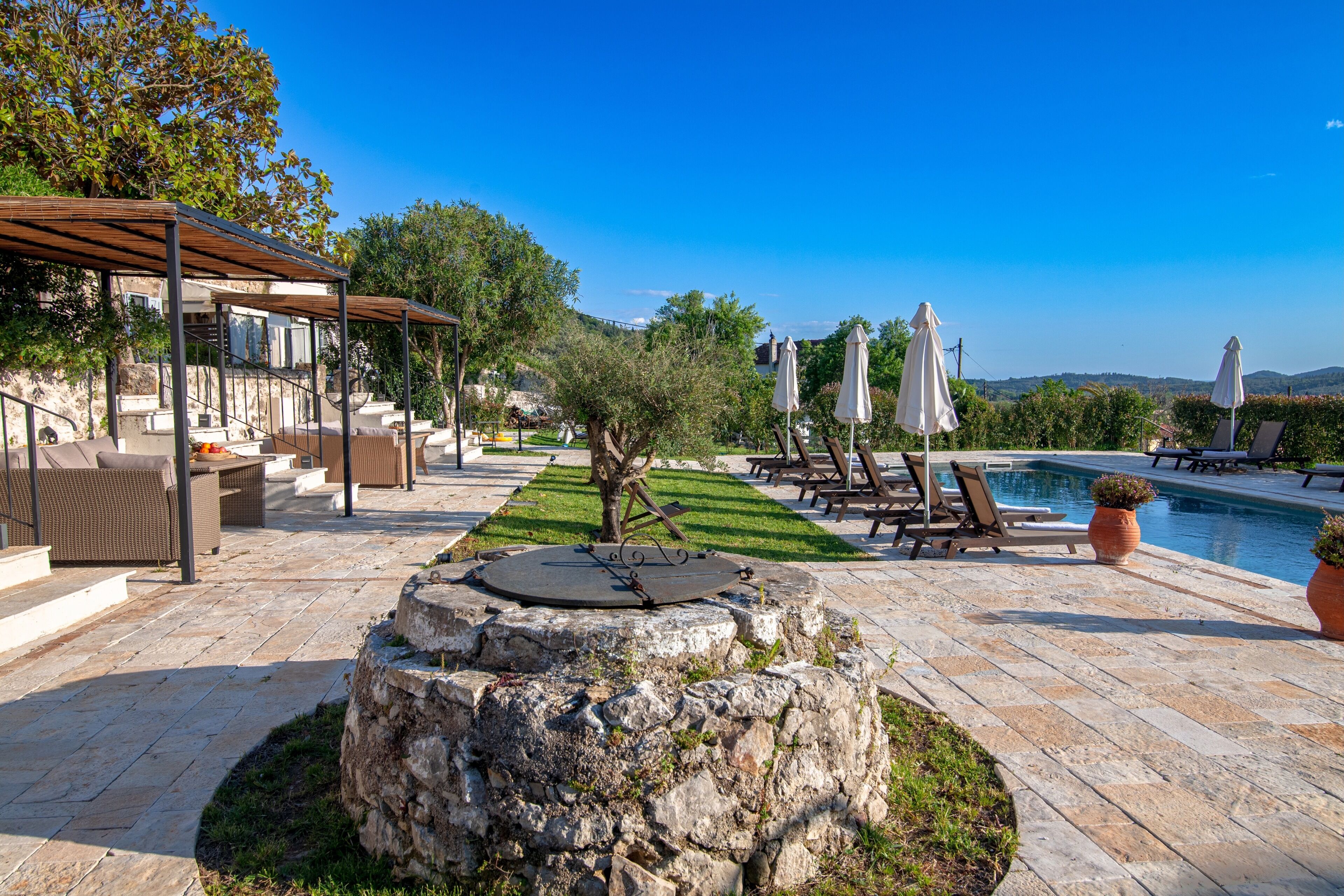Ein Poolbereich mit Liegestühlen, Sonnenschirmen und einer Pergola.