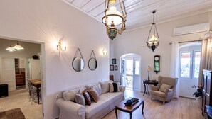 Un ampio soggiorno con divano, tavolino e lampadario. C'è una zona pranzo con tavolo e sedie, e un orologio appeso al muro.