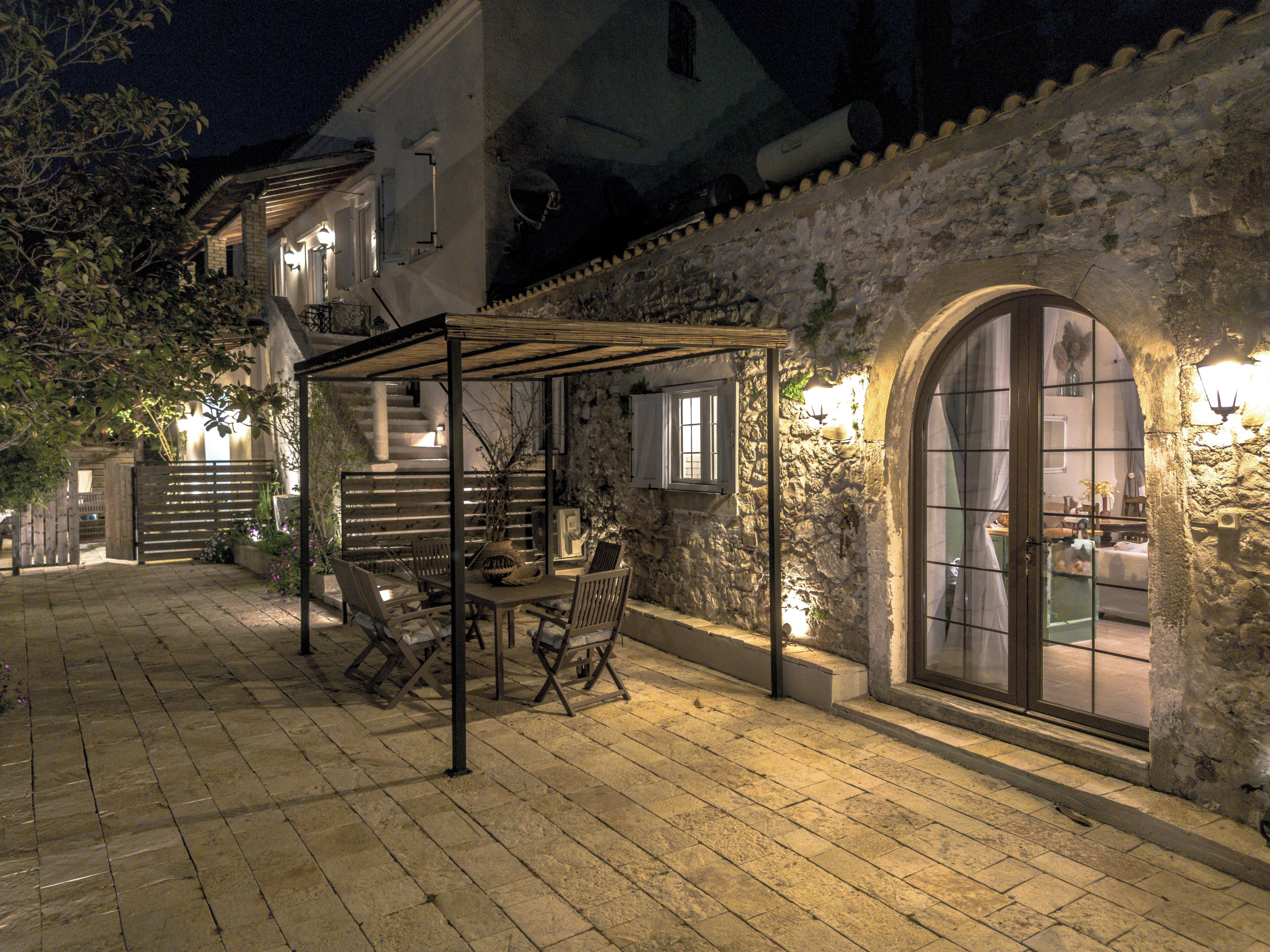 A courtyard with a pergola, outdoor seating, stone walls, and a large arched window.