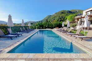 A swimming pool with lounge chairs and umbrellas, surrounded by greenery and mountains. - Marcora Historic Mansion (Corfu)