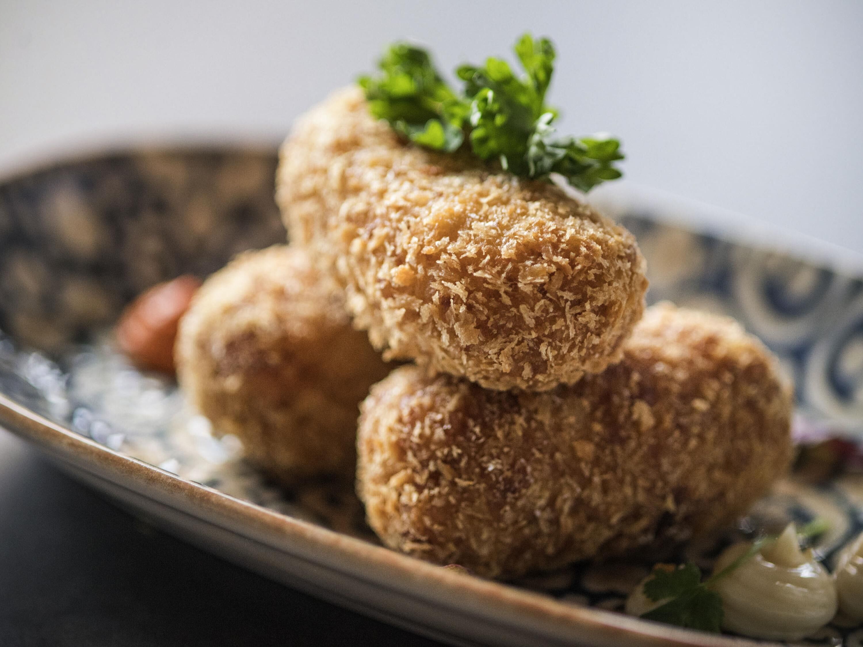 Un plato con porciones de comida empanizada y frita, posiblemente croquetas, adornado con perejil, sobre un plato decorativo.