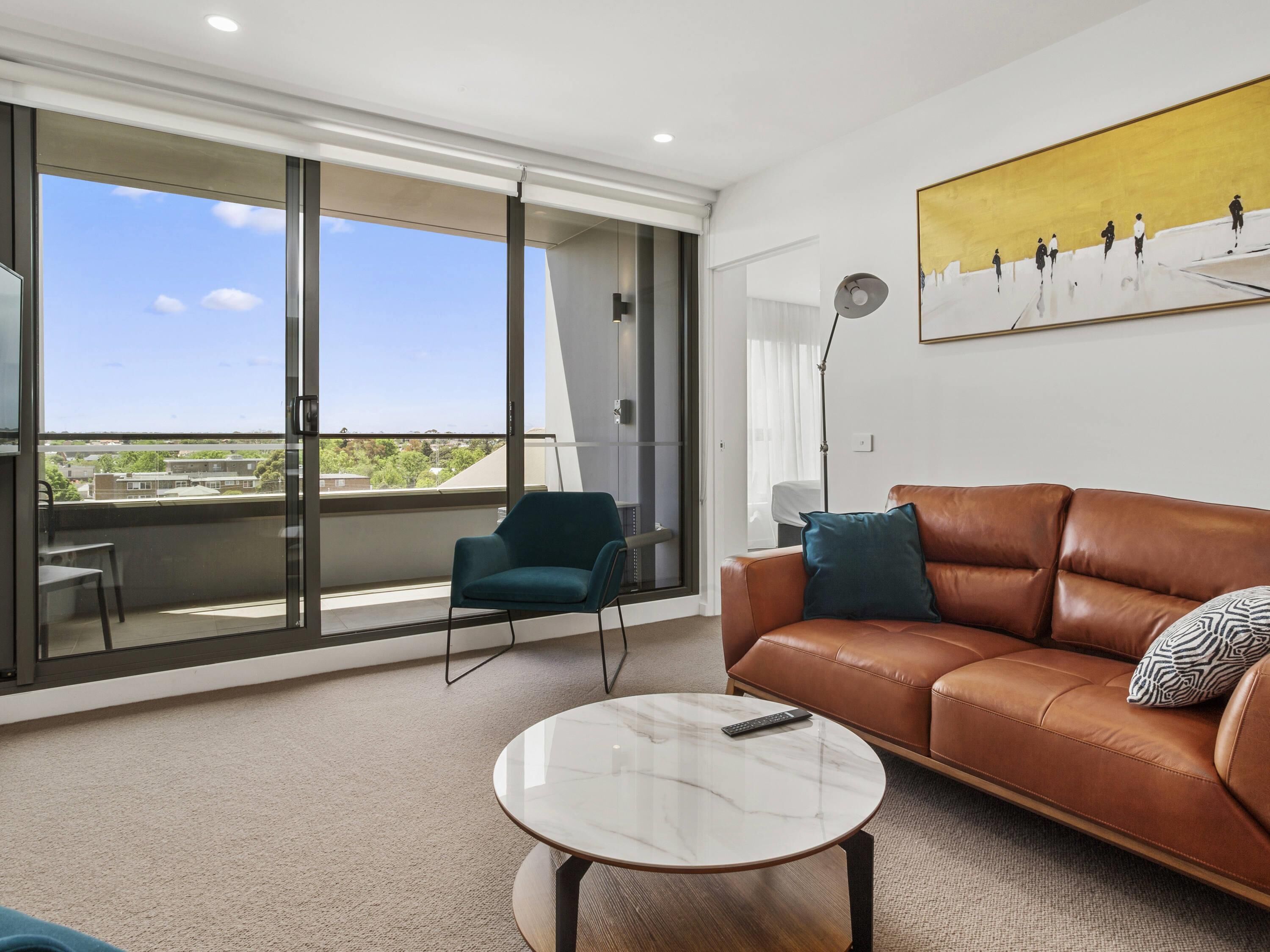 A modern living room with a leather sofa, a teal armchair, and a marble coffee table.