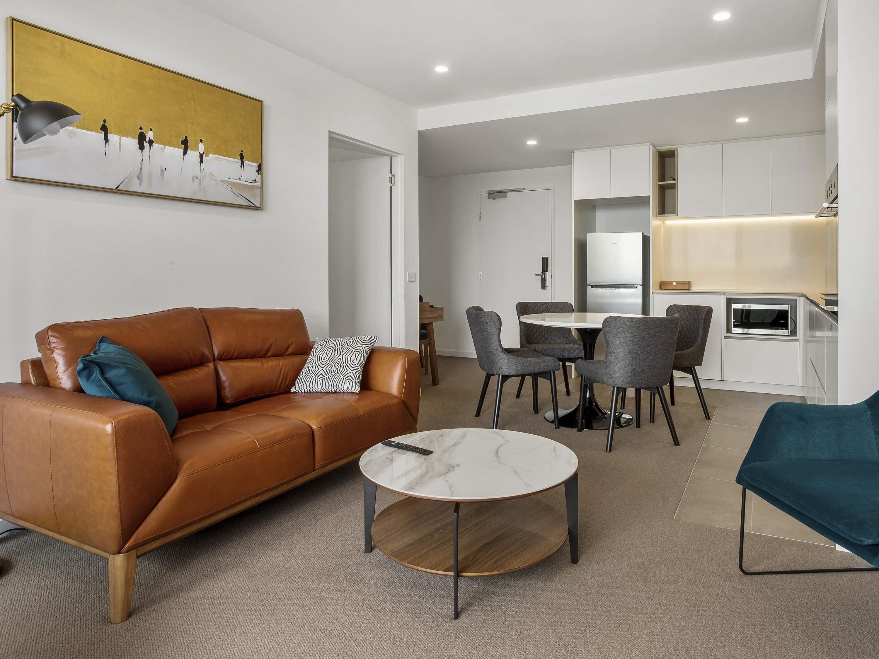 A modern living room with a brown leather sofa, a round coffee table, and a dining area with grey chairs.
