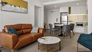 A modern living room with a brown leather sofa, a round coffee table, and a dining area with grey chairs.