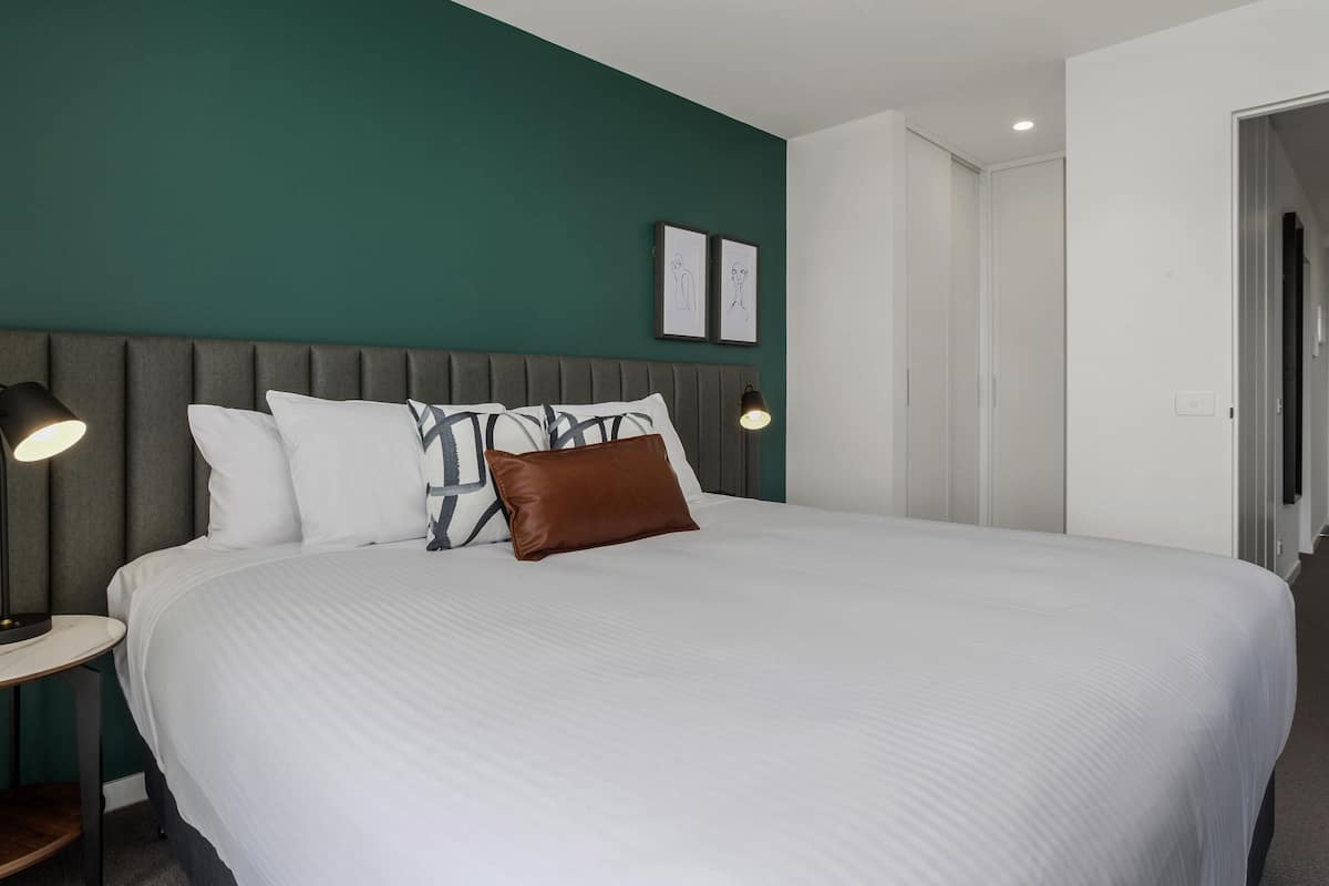 A modern hotel room with a large bed, two bedside lamps, and a green accent wall.