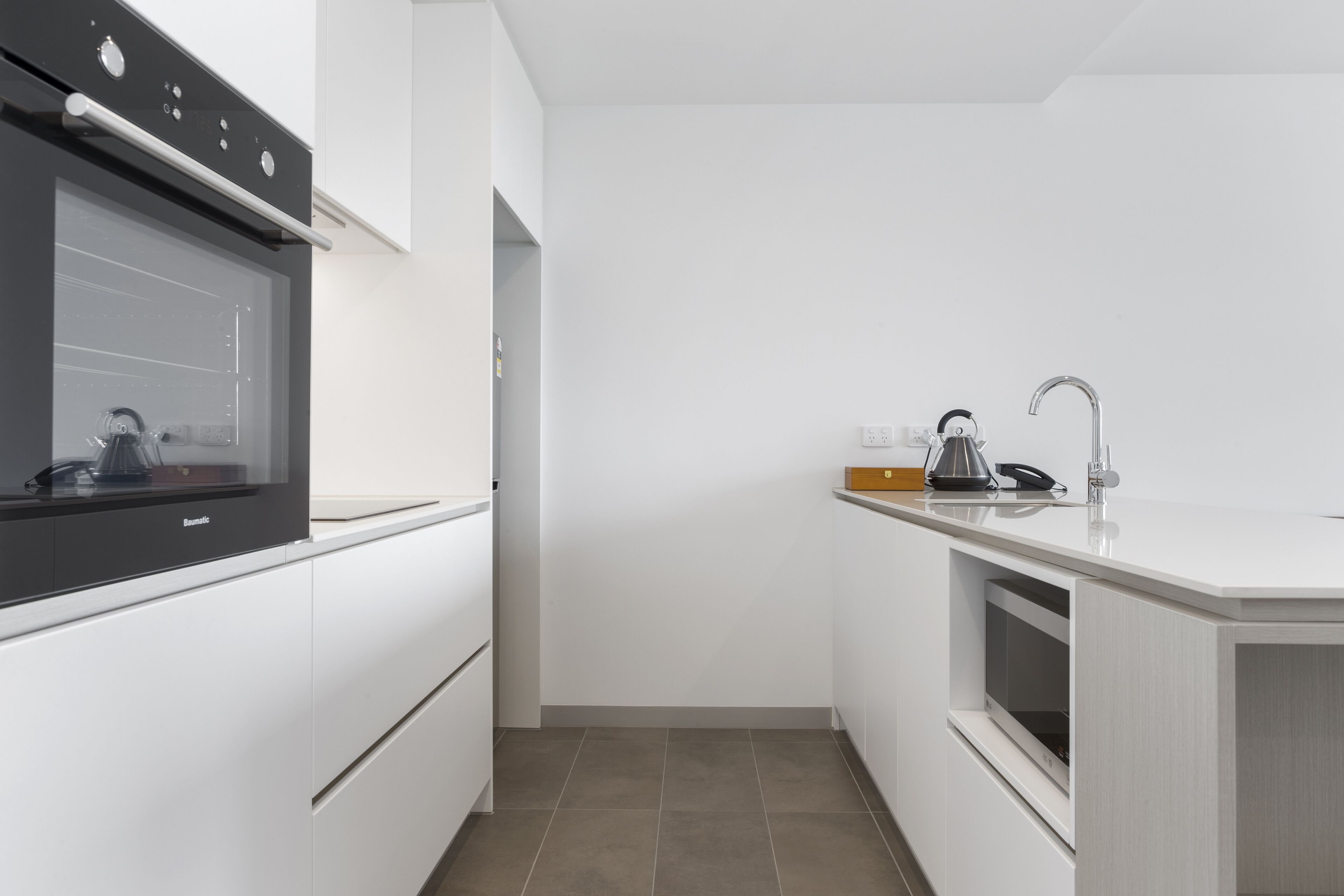 A modern kitchen with white cabinetry, a built-in oven, a sink, and a countertop with a kettle.