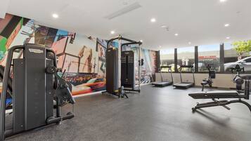 A gym with various exercise equipment, a mural on the wall, and large windows.